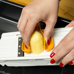 Mână taie o cartof pe o răzătoare pentru legume, ținut cu un protector galben pentru degete.