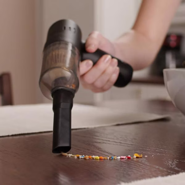 O persoană aspiră cu un aspirator de mână compact mărgele colorate sau firimituri de pe masă.